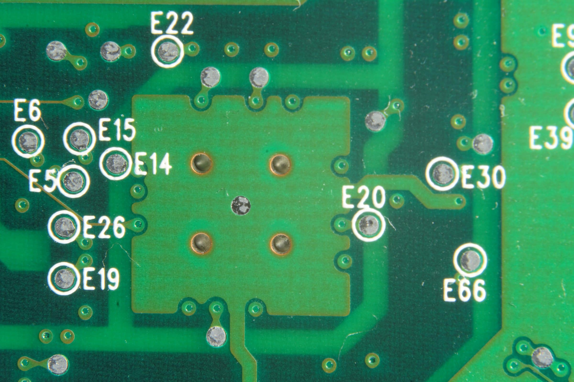 A close view of a green printed circuit board, its surface marked with component codes and soldering pads.